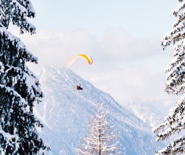 Person soaring on parachute through the snowy valley Person soaring on parachute through the snowy valley